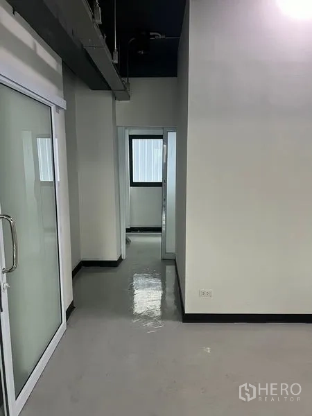 零售空间 出租在Watthana, Bangkok - 走廊与推拉玻璃入口，内有带窗的小型办公室。