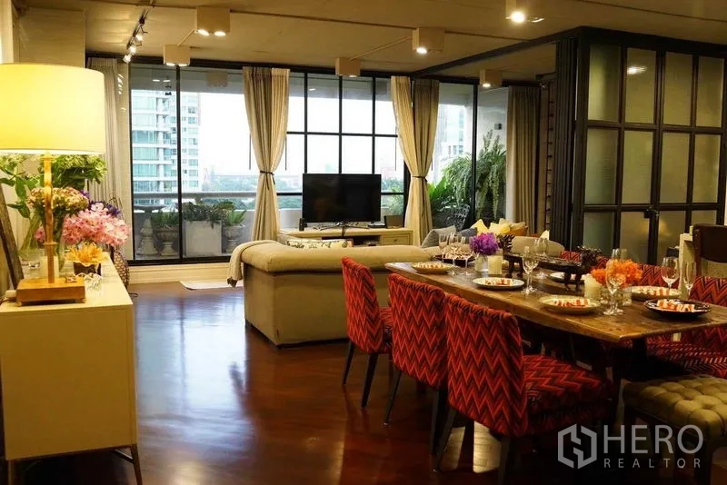 Condominium for sale in Pathum Wan, Bangkok - Dining table set for six beside the living area, opening to a balcony with tall windows.