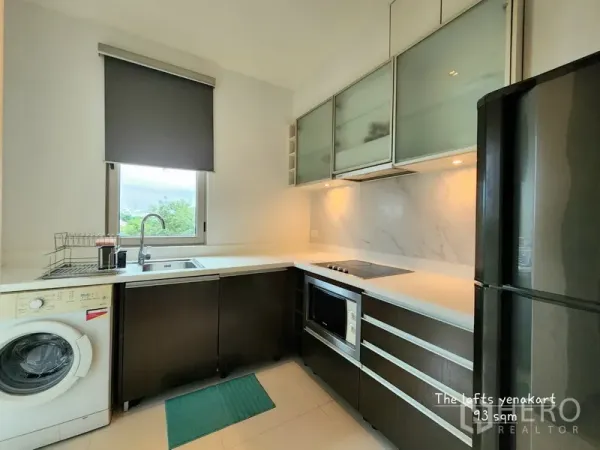 Condominium for rent in Yan Nawa, Bangkok - Modern U-shaped kitchen with white countertops, window, washing machine, oven, cooktop, and full-size refrigerator.