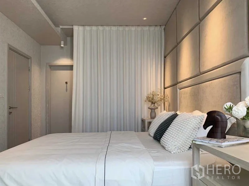 Condominium for rent or sale in Watthana, Bangkok - Bedroom angle showing white curtains, doorway and bedside table decor.