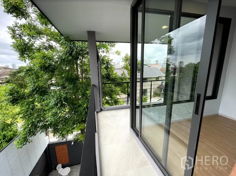 Detached House for sale in Watthana, Bangkok - Covered balcony with sliding glass doors and leafy outlook.