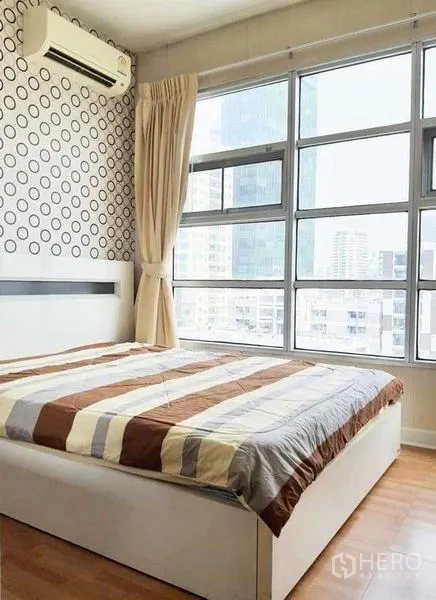 公寓 出租在Ratchathewi, Bangkok - 卧室大面积窗户观城市景观，条纹被套，圆点墙面与空调。