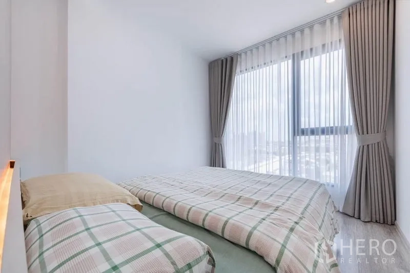 Condominium for rent in Bang Na, Bangkok - Primary bedroom with large corner windows, sheer curtains, and abundant natural light.