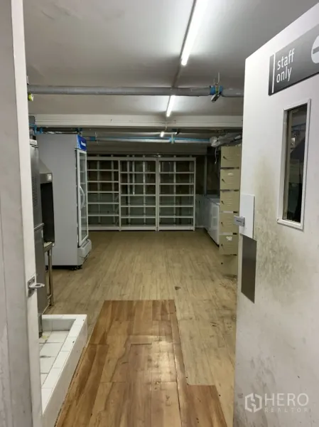 零售空间 出租在Sathon, Bangkok - 从员工通道望向库房，木纹地面、冰柜与墙面货架清晰可见。