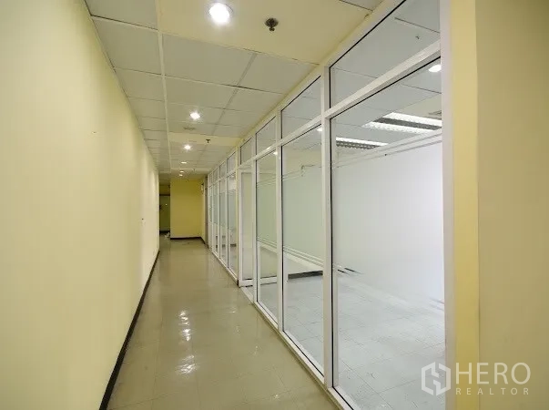 สำนักงาน ให้เช่าในWatthana, Bangkok - โถงทางเดินยาวขนาบผนังกระจกของห้องทำงาน ไฟดาวน์ไลท์และพื้นกระเบื้องมันเงา