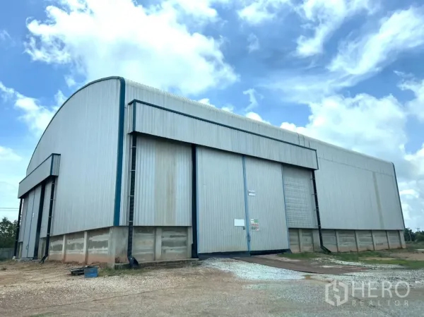 Warehouse for rent in Ban Pho, Chachoengsao - Steel-clad warehouse exterior with high sliding doors and a gravel yard under a bright sky.
