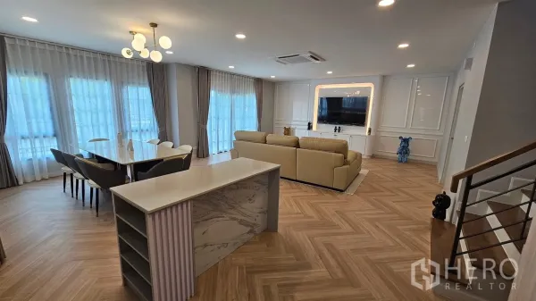 Detached House for rent or sale in Bang Phli, Samut Prakan - Bright open-plan living and dining area with large windows, sheer curtains, herringbone wood floors, sectional sofa and TV wall.