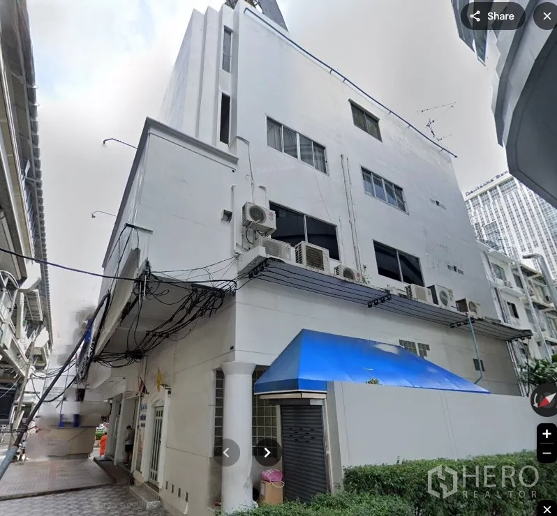 店屋 for rent in Pathum Wan, Bangkok - 转角白色多层商铺外观，配蓝色雨篷、卷闸门、侧巷通道及多组外置空调机组。