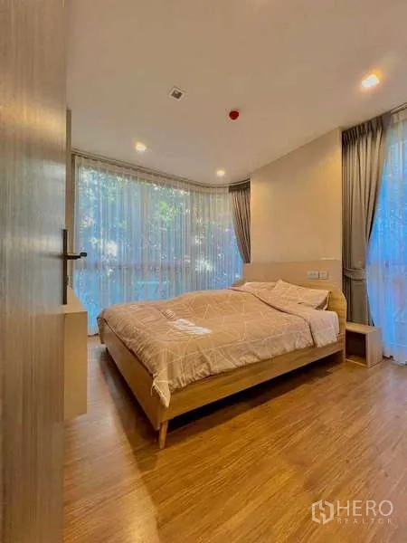 Condominium for sale in Watthana, Bangkok - Primary bedroom with large corner windows, curtains and wood floors.