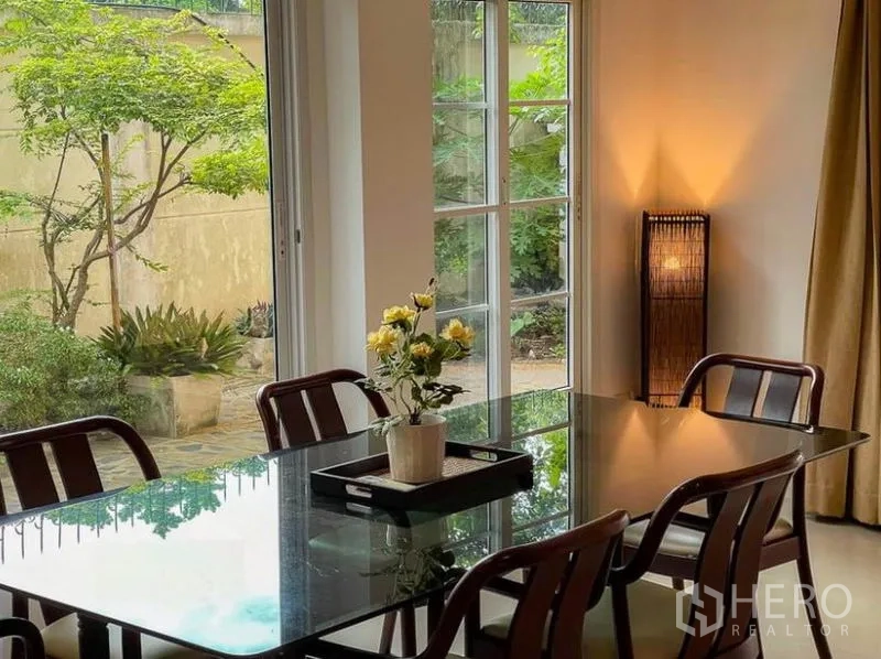 Townhouse for rent in Phasi Charoen, Bangkok - Dining table beside tall windows overlooking the garden patio.