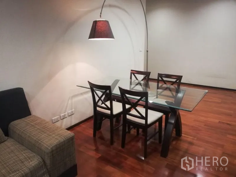 Condominium for rent in Watthana, Bangkok - Dining area with a glass table for four under an arc floor lamp beside the sofa.