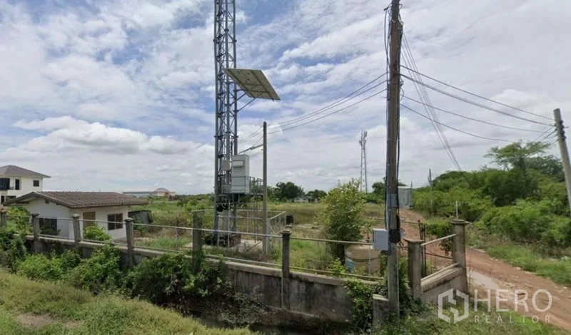 Land for sale in Bang Sao Thong, Samut Prakan - Power poles, cables and a telecom mast beside open industrial land and a compacted dirt road.