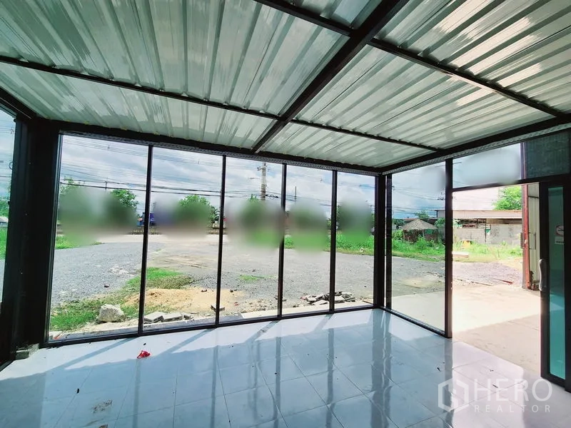 货栈 出租在Sam Phran, Nakhon Pathom - 仓库前端的玻璃办公区，落地窗面向宽阔的碎石空地与绿化。