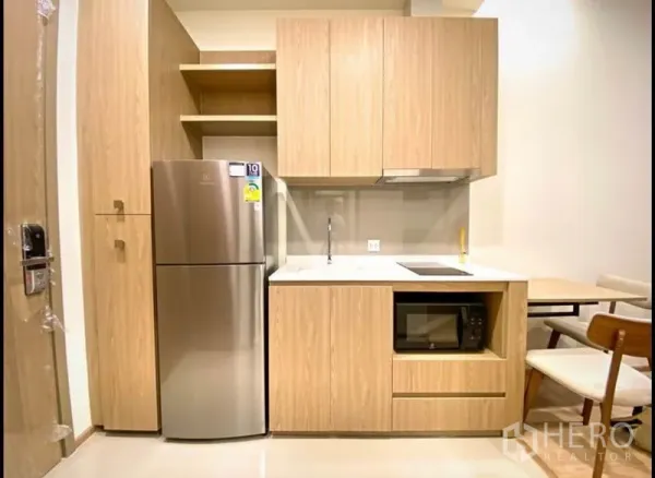 Condominium for sale in Huai Khwang, Bangkok - Compact kitchenette with light wood cabinets, stainless refrigerator, cooktop and microwave.