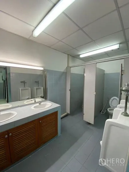 办公空间 出租 - 办公楼公共卫生间，双洗手台、多个小便池与隔间，荧光灯照明。