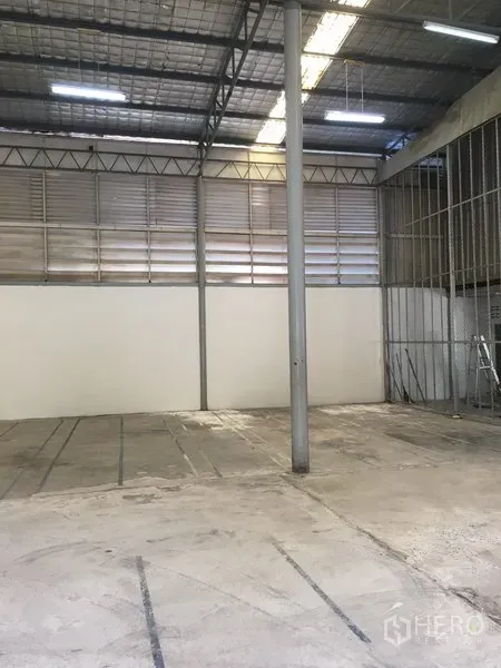 Warehouse for rent in Suan Luang, Bangkok - Empty warehouse bay with concrete floor, metal louvered vents, and a central steel column under bright lighting.