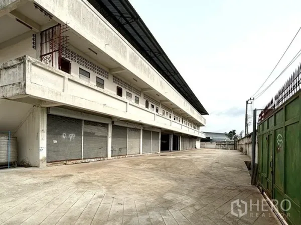 Warehouse for rent in Bang Khun Thian, Bangkok - Row of roller-shutter loading bays beside a secure green gate and driveway.