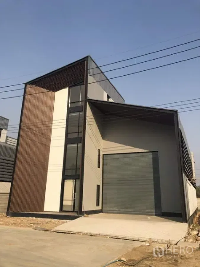 โรงงาน ขายในThanyaburi, Pathum Thani - ด้านนอกอาคารโรงงานสไตล์โมเดิร์น มีกันสาดลานโหลดและประตูม้วนขนาดใหญ่