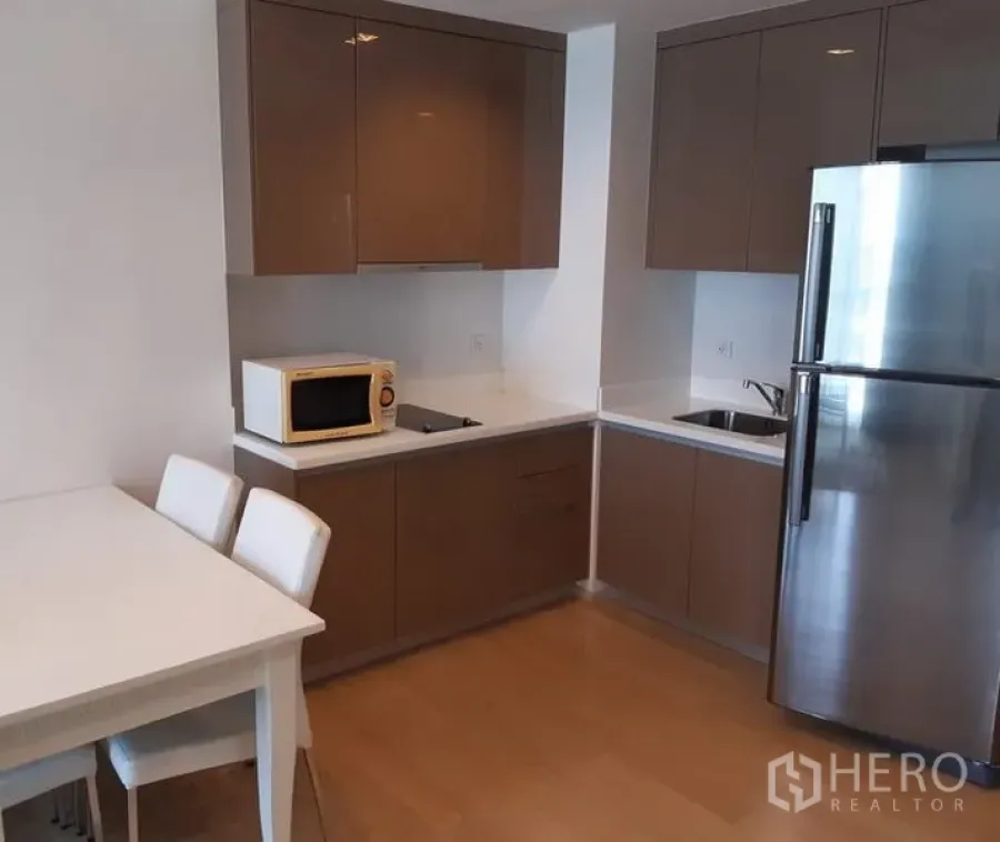 คอนโด ให้เช่าในKhlong Toei, Bangkok - ครัวรูปตัวแอลพร้อมตู้บิวท์อินเงางาม ตู้เย็นสแตนเลส ไมโครเวฟ และชุดโต๊ะทานอาหารภายในคอนโด