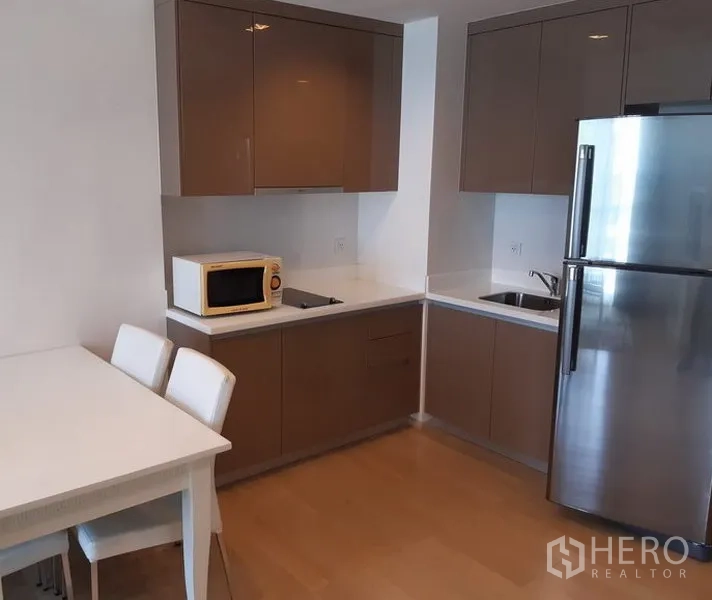 คอนโด ให้เช่าในKhlong Toei, Bangkok - ครัวรูปตัวแอลพร้อมตู้บิวท์อินเงางาม ตู้เย็นสแตนเลส ไมโครเวฟ และชุดโต๊ะทานอาหารภายในคอนโด