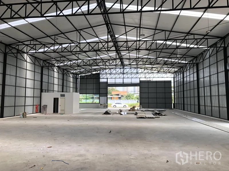 Warehouse for rent in Pak Kret, Nonthaburi - Expansive warehouse floor under skylit roof with wide loading doors opening to the yard.