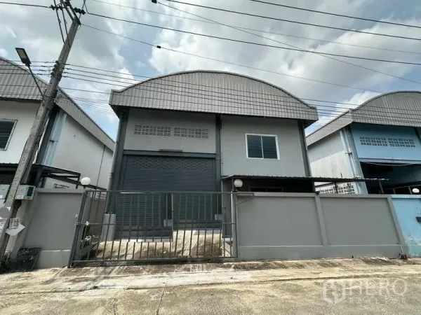 Warehouse for rent in Pak Kret, Nonthaburi - Gated modern warehouse facade with wide roller shutter and curved metal roof in Pak Kret.
