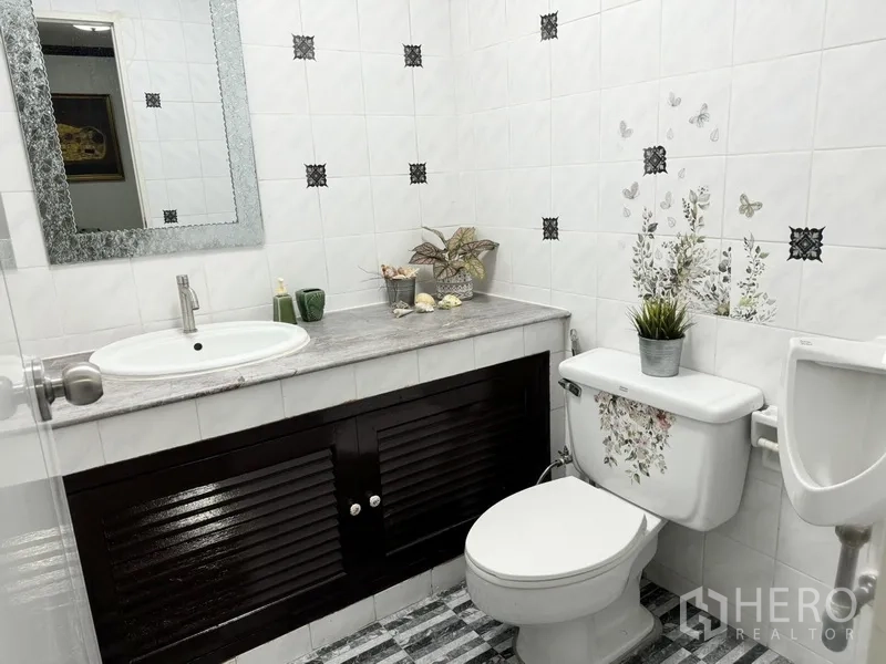 联排别墅 出租在Prawet, Bangkok - 整洁卫生间，盥洗台、镜子与带花纹贴纸的坐便器。