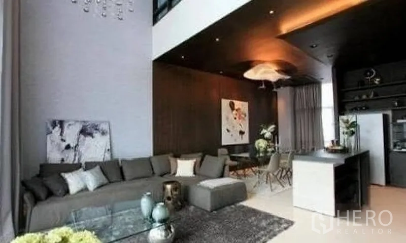 Townhouse for rent in Watthana, Bangkok - Double-height lounge with dark feature wall, large sofa and open dining area.