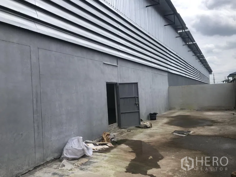 工厂 出租在Sai Noi, Nonthaburi - 厂房后方服务庭院，实体围墙、侧门与地面排水。