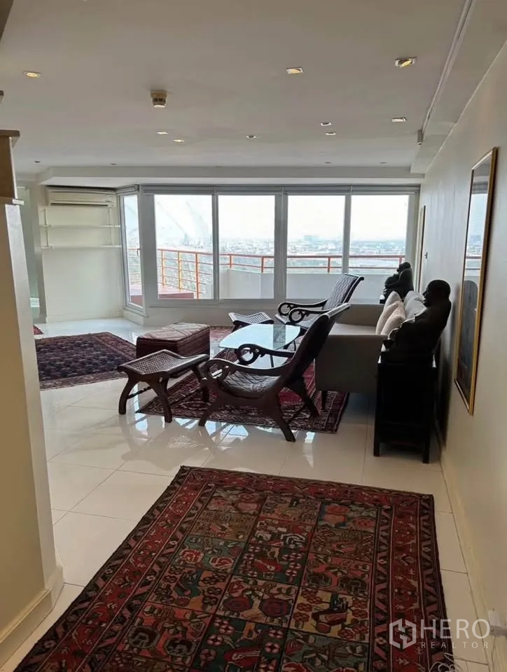 Condominium for rent or sale in Yan Nawa, Bangkok - Bright living room with floor-to-ceiling windows, balcony access and city views, furnished with classic wooden seating.