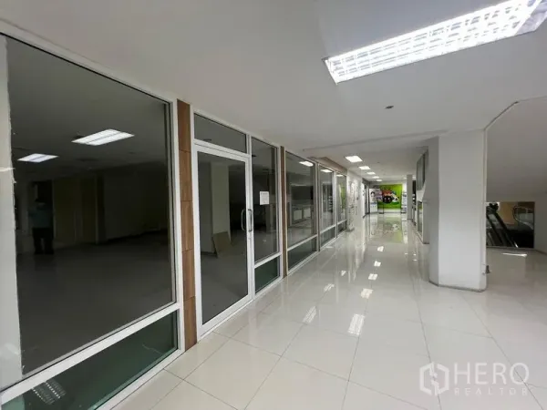 零售空间 出租 - 采光充足的商场走廊，多家玻璃店面与光亮瓷砖地面，前方有扶梯