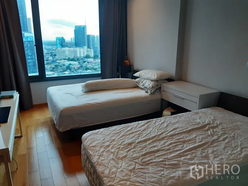 Condominium for rent or sale in Khlong Toei, Bangkok - Bedroom with twin beds and a large window overlooking the Bangkok skyline.