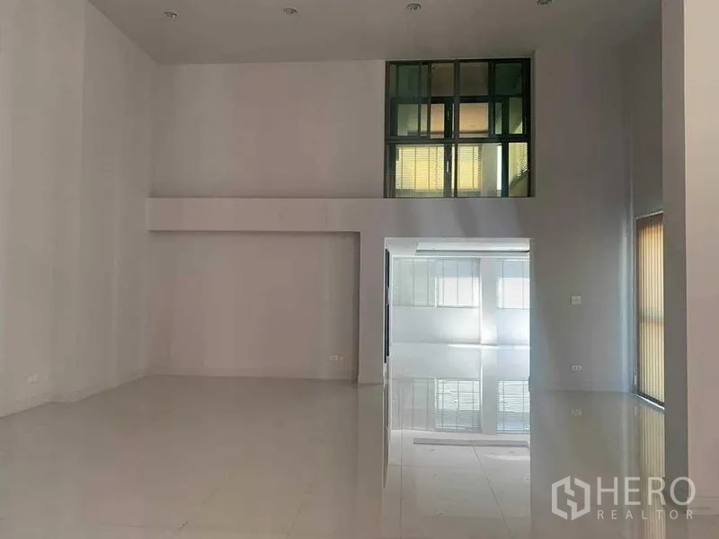 Townhouse for rent or sale in Yan Nawa, Bangkok - Double-height living area with glossy white flooring and interior windows.
