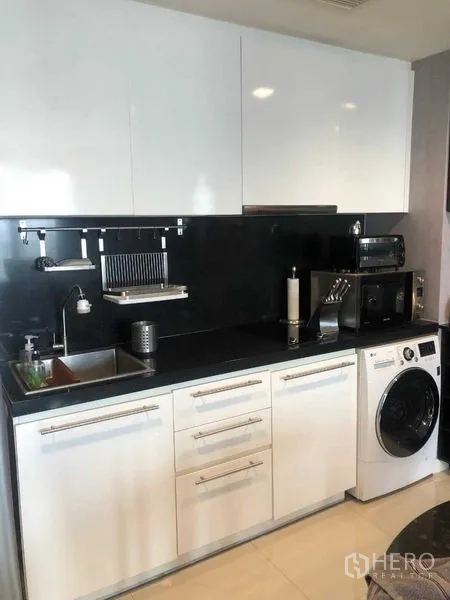 公寓 出租或出售在Bang Kho Laem, Bangkok - 简洁厨房，白色高光柜体、黑色挡板与室内洗衣机。