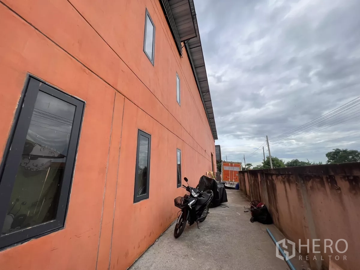 คลังสินค้า ให้เช่าหรือขายในLat Krabang, Bangkok - ทางเดินข้างอาคาร ผนังสีส้มมีช่องหน้าต่างและร่มชายคา มีรถจักรยานยนต์จอด