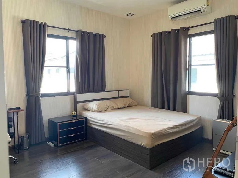 Detached House for rent or sale in Bang Phli, Samut Prakan - Bright bedroom with double bed, two windows, dark curtains and wood floors.