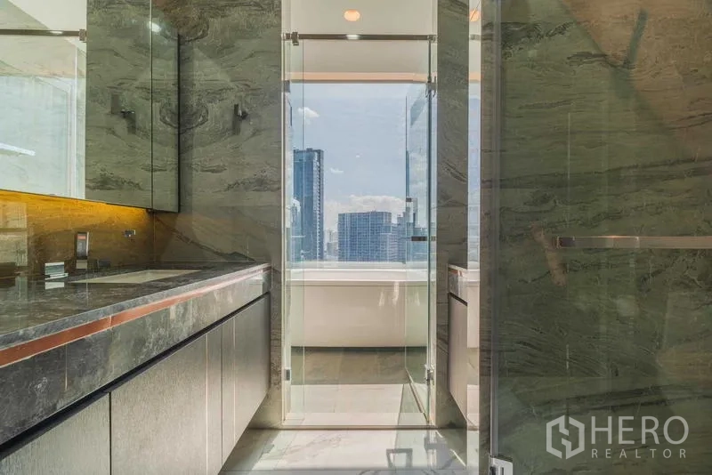 Condominium for rent or sale - Double-vanity marble bathroom leading to a glass door and soaking tub with skyline view.