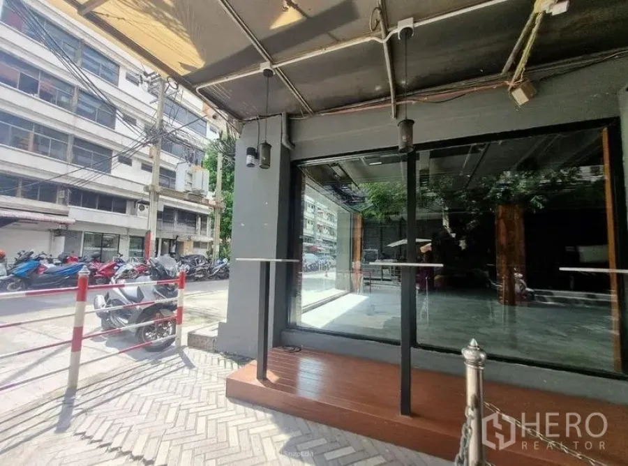 零售空间 出租在Bang Rak, Bangkok - 玻璃店面特写，遮棚下的抬高木平台与铺砖人行道。