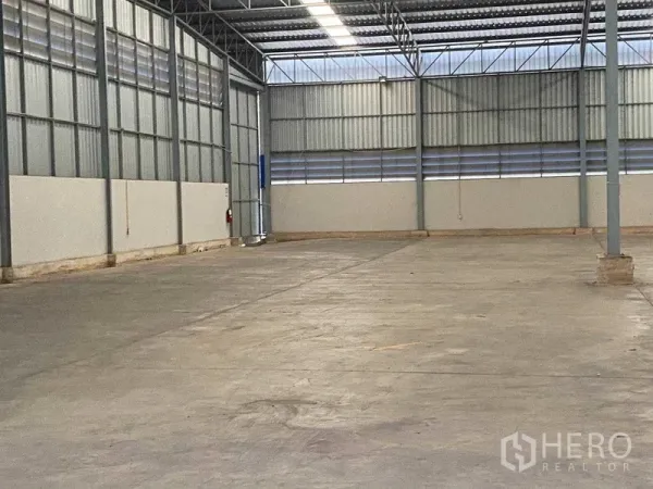 Warehouse for rent in Lat Krabang, Bangkok - Corner of empty warehouse featuring ventilation slats, steel columns and emergency equipment on concrete flooring.