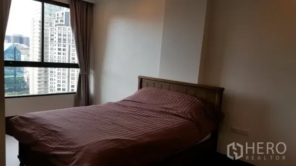 Condominium for rent in Sathon, Bangkok - Bright bedroom with large window and city view, queen bed and curtains.