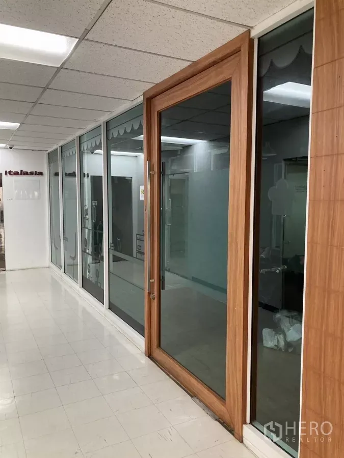 Office Space for rent in Watthana, Bangkok - Corridor with glass-front offices and a wood-framed door in a Watthana Bangkok workspace.