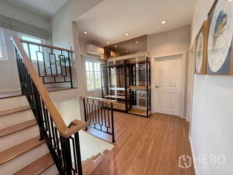 独立式住宅 出售在Bang Khen, Bangkok - 楼梯厅，黑色金属栏杆、木踏步与明亮窗边展示柜。