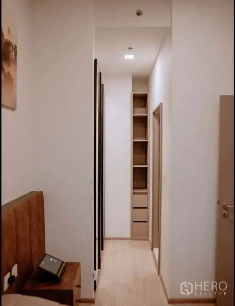 Condominium for sale in Huai Khwang, Bangkok - Narrow corridor with tall open shelving and mirrored wardrobe for storage.