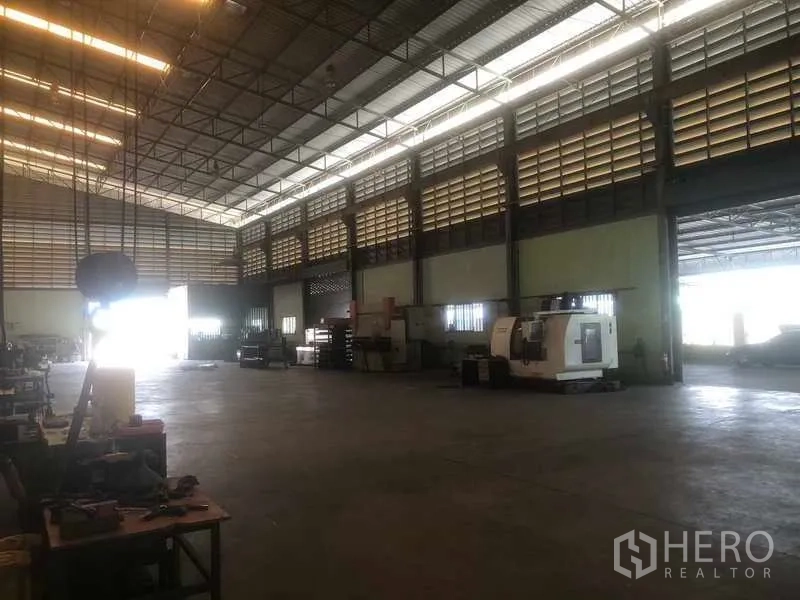 Warehouse for sale in Rayong - High-ceiling factory floor with machinery and drive-through access.