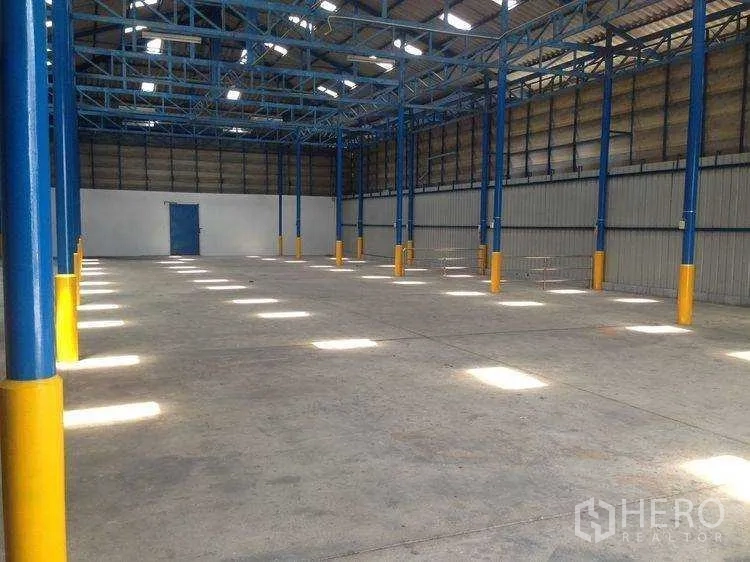 Warehouse for rent in Bang Kapi, Bangkok - Long clear-span bay with blue trusses, yellow column guards and a rear access door.