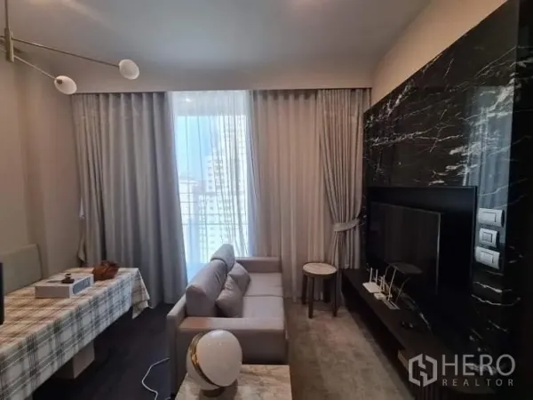 Condominium for rent in Watthana, Bangkok - Modern living room featuring a dark marble TV wall, sofa, and sheer curtains.