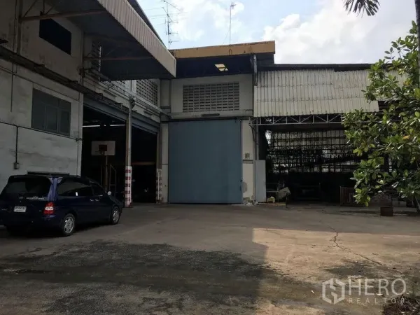 Warehouse for rent in Phra Pradaeng, Samut Prakan - Industrial warehouse entrance in Phra Pradaeng with tall blue door, covered loading bays and a spacious concrete yard.