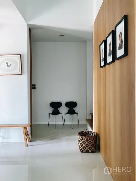 Detached House for sale in Bang Kapi, Bangkok - Minimalist hallway with wood panel wall, bench, and framed photos.