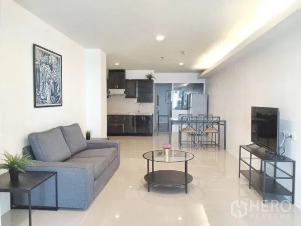 คอนโด ให้เช่าในKhlong Toei, Bangkok - โซนพักผ่อนแบบเปิดโล่ง โซฟาสีเทา โต๊ะกลางกลม ชั้นวางทีวี เชื่อมกับครัวและโต๊ะกินข้าว คอนโดสุขุมวิท
