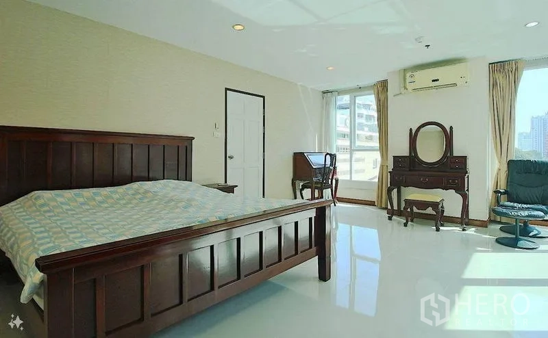 Condominium for sale in Watthana, Bangkok - Spacious master bedroom with wood furniture, desk and city views from corner windows.